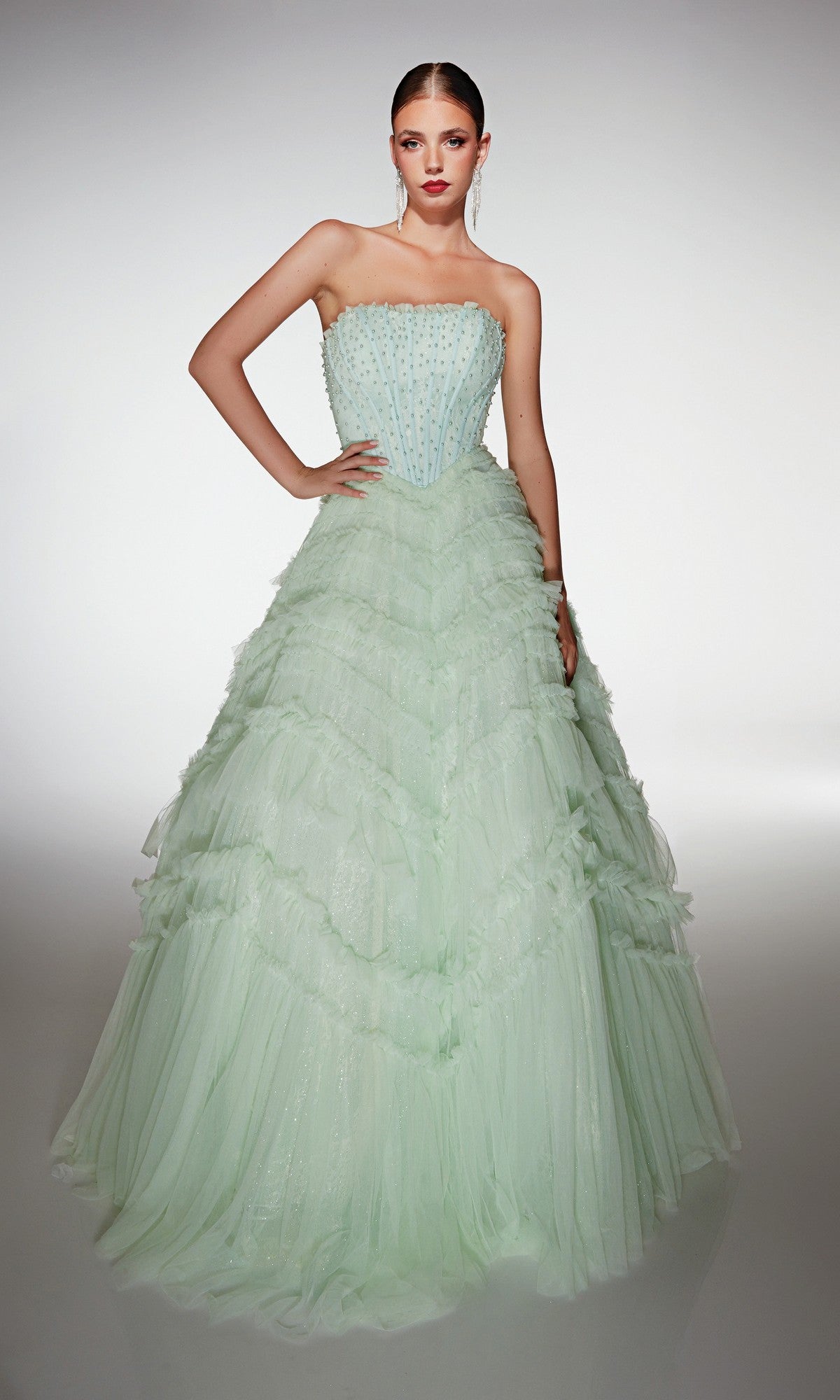 A woman poses in the Alyce 62208 long prom dress, a mint green strapless ballgown with a fitted beaded bodice and dramatic tulle ruffle skirt, set in a plain studio background.